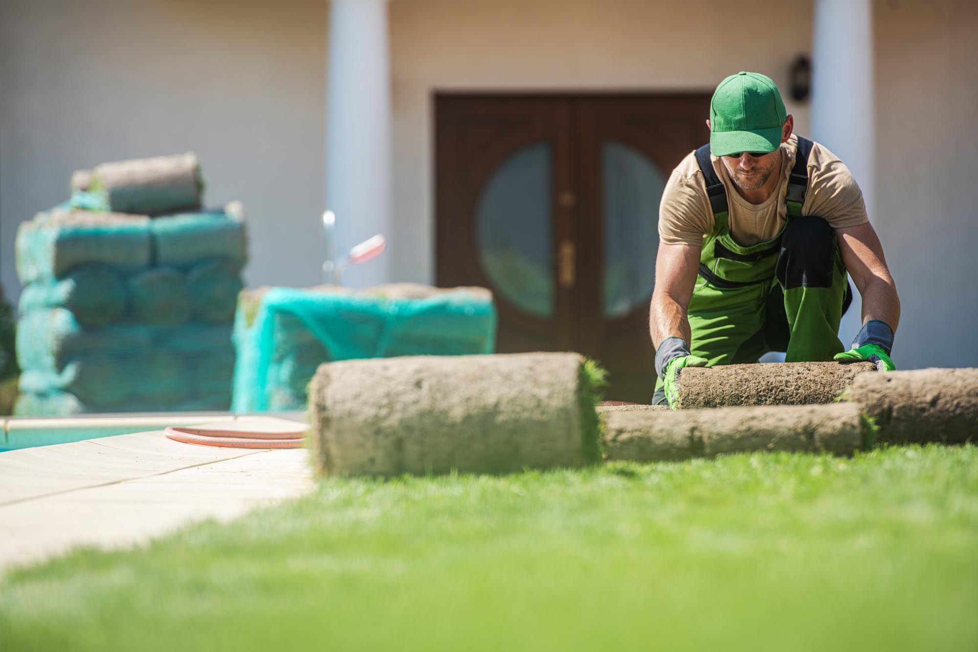 A worker in green overalls is mowing a lawn, surrounded by lush grass and trees in a sunny outdoor setting by All Season Utah.