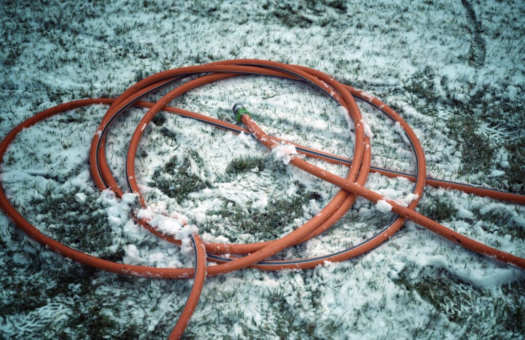 Coiled orange garden hose lying on snowy ground covered with light snow patches.
